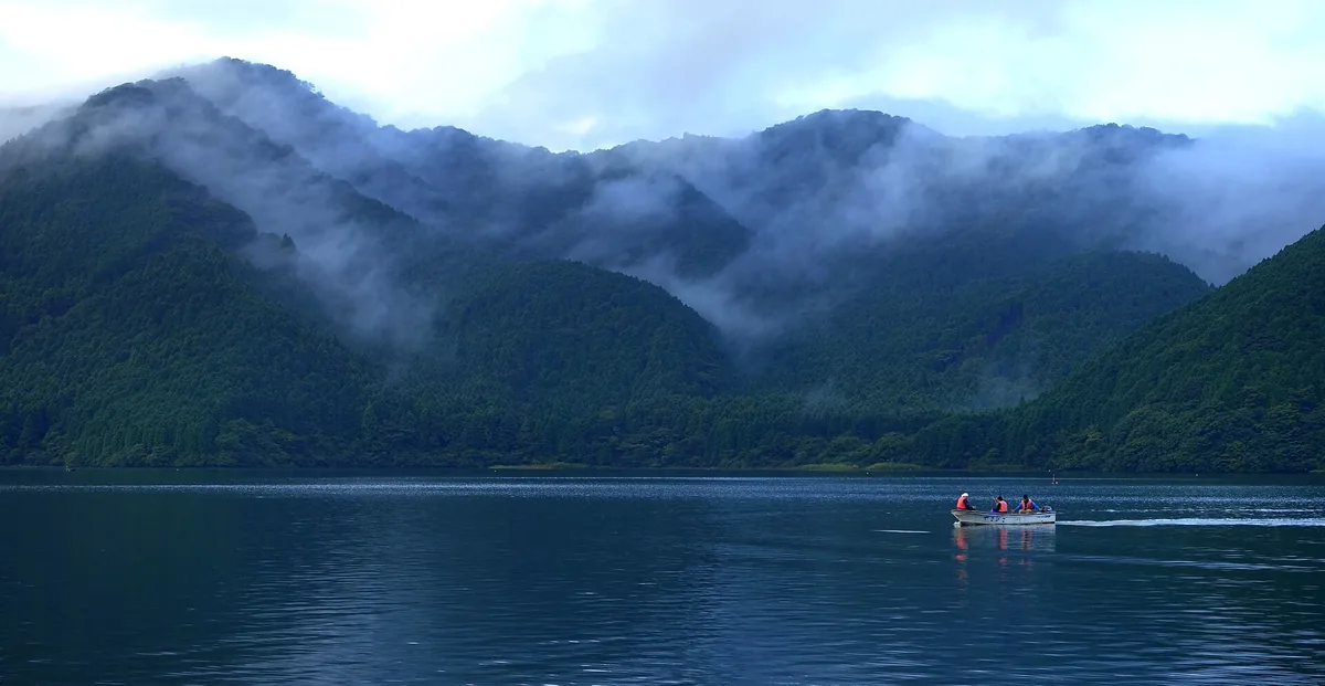 Lake Ashi beneath misty forested mountains in Hakone with a small boat on the water