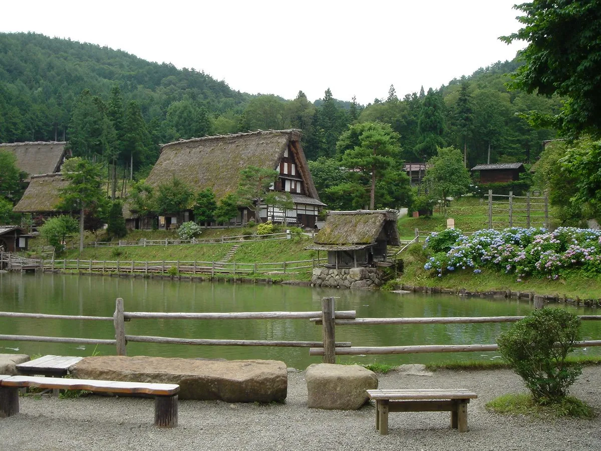 Traditional thatched buildings and a waterwheel beside the pond at Hida Folk Village