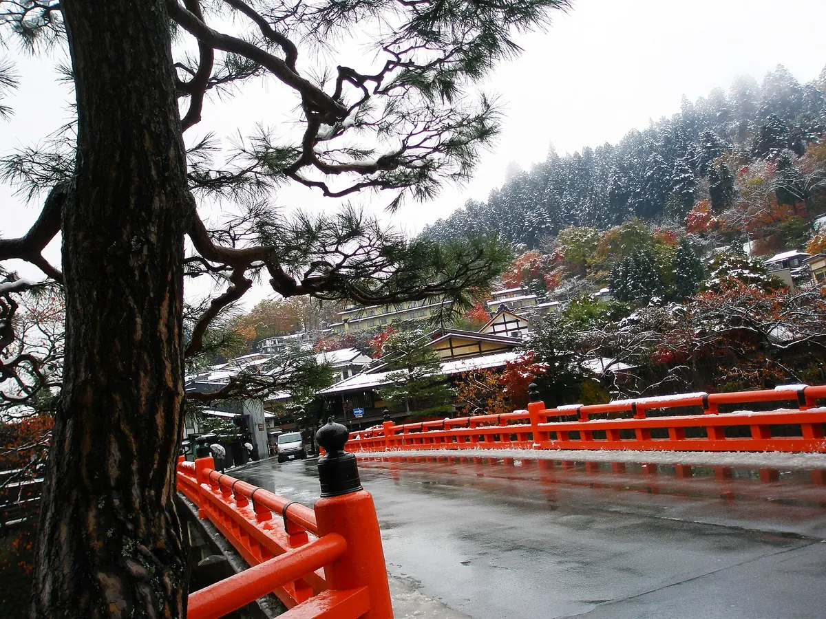 Red Nakabashi Bridge in Takayama surrounded by autumn foliage and early snow